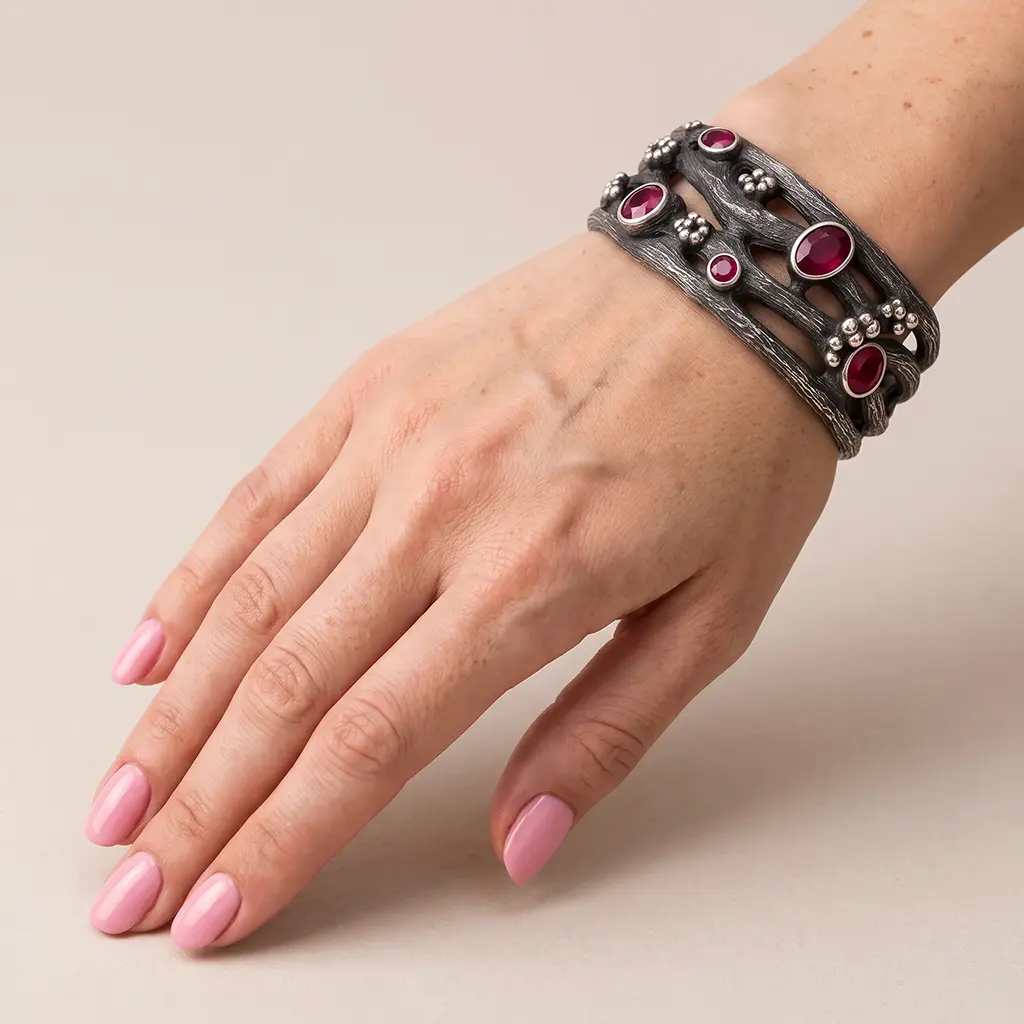 Wide garnet cuff bracelet in black sterling silver worn on a woman's wrist, beige background