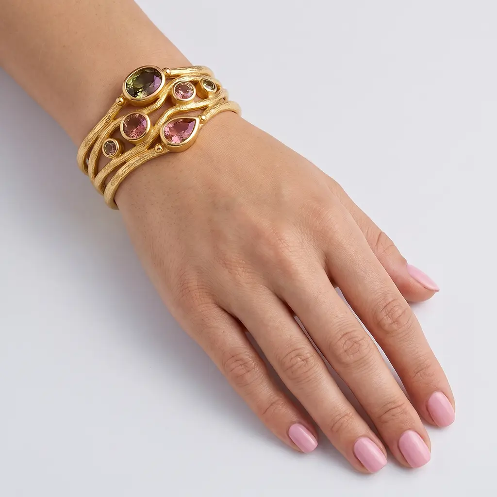 Solid gold bracelet on a woman's wrist: 14K cuff of four textured rows, lab-grown zultanite in pink and olive tones