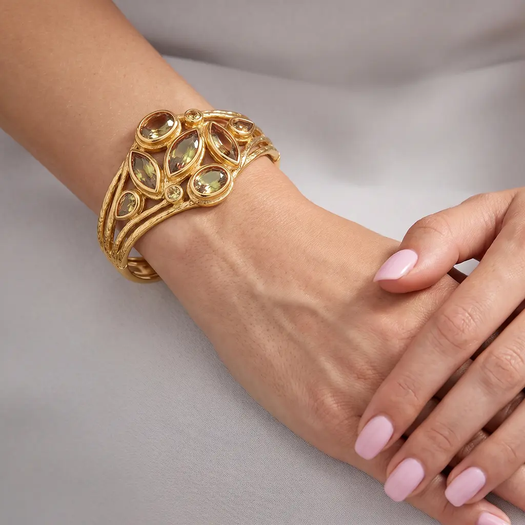 Wide gold cuff bracelet with lab-grown zultanite marquises and ovals on a woman's wrist, hands folded