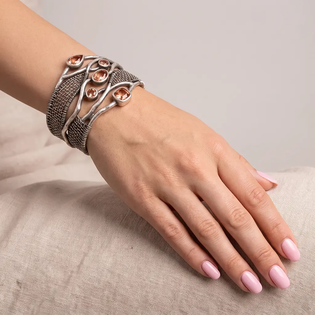 Silver wire weave cuff with lab-grown zultanite in warm light, worn on a woman's wrist, hand resting on linen