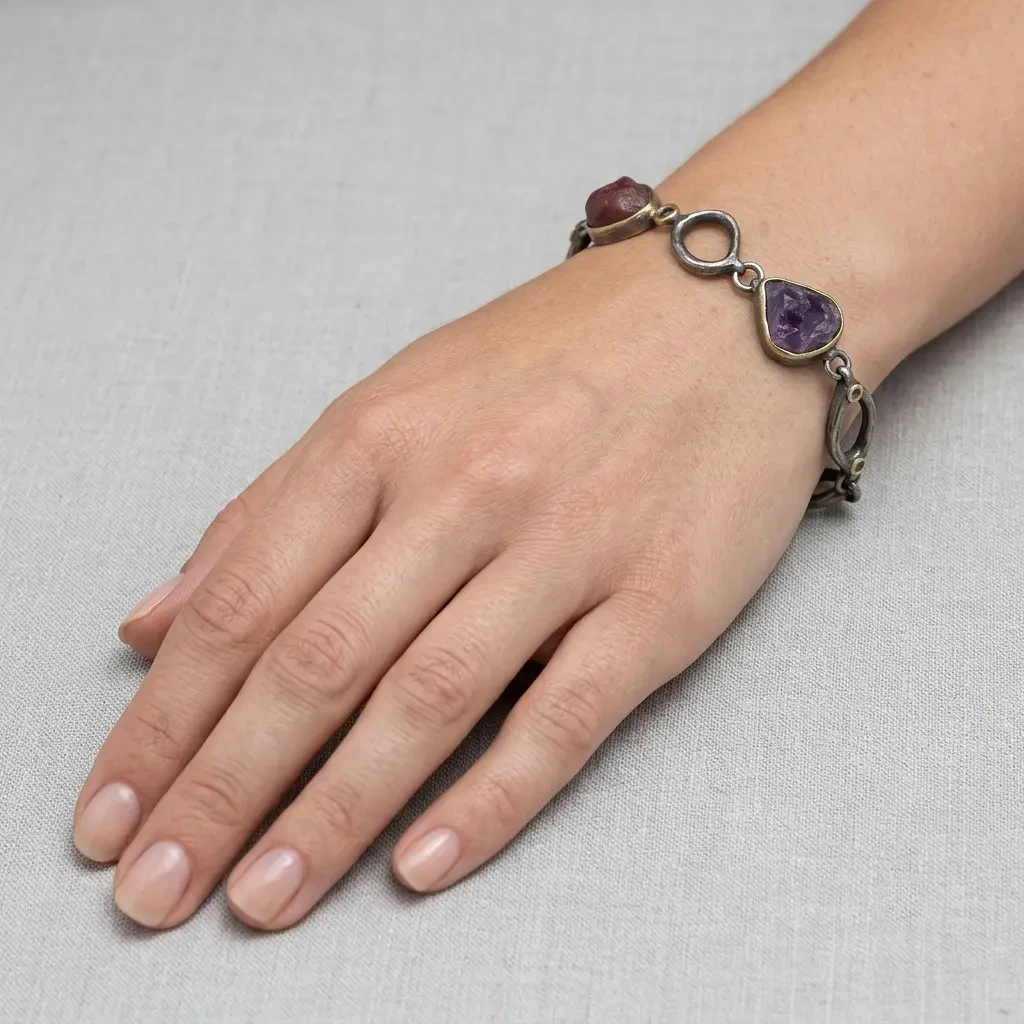 Women's bracelet of black oxidized silver links with raw ruby and amethyst, worn on the wrist over grey linen
