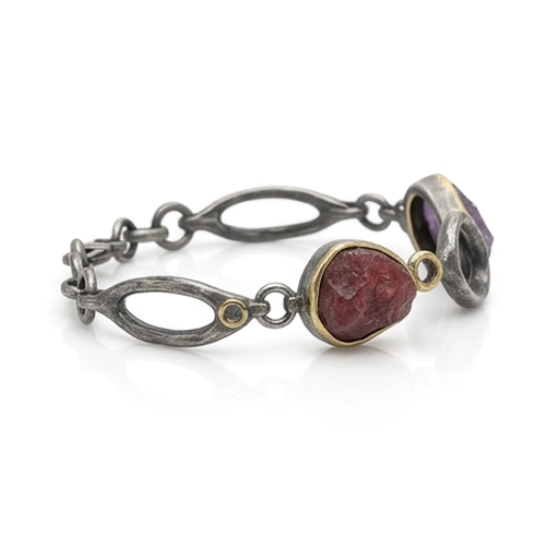 Sterling silver link bracelet at an angle, showing open oval links, the raw ruby bezel and small round rings
