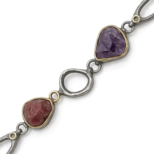 Close-up of the multi gemstone bracelet with raw amethyst and raw ruby in gold-tone bezels between blackened silver links